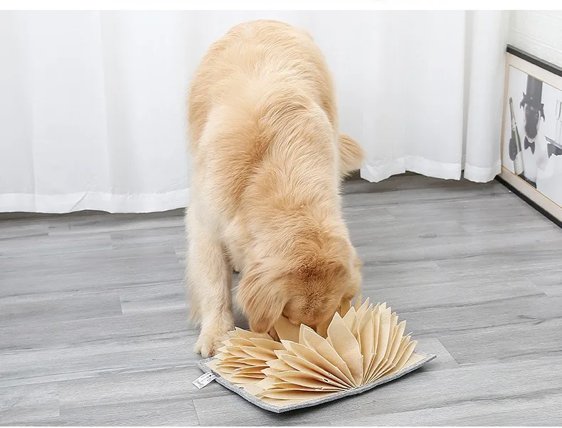 Dog using a beige accordion snuffle mat on a wood floor at home
